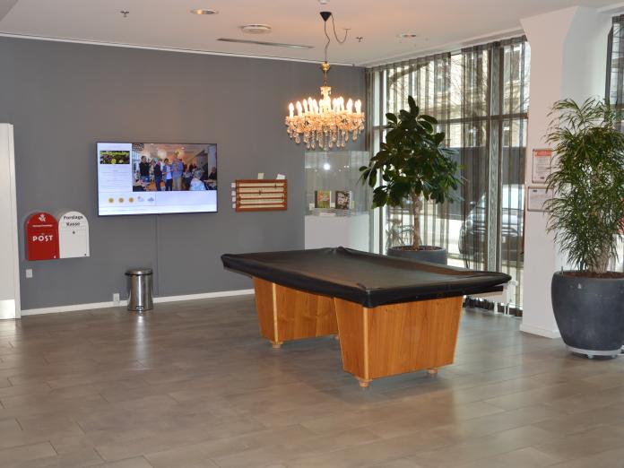 Forhal med billardbord. Grå vægge, to store planter, to postkasser på væggene og en lysekrone.