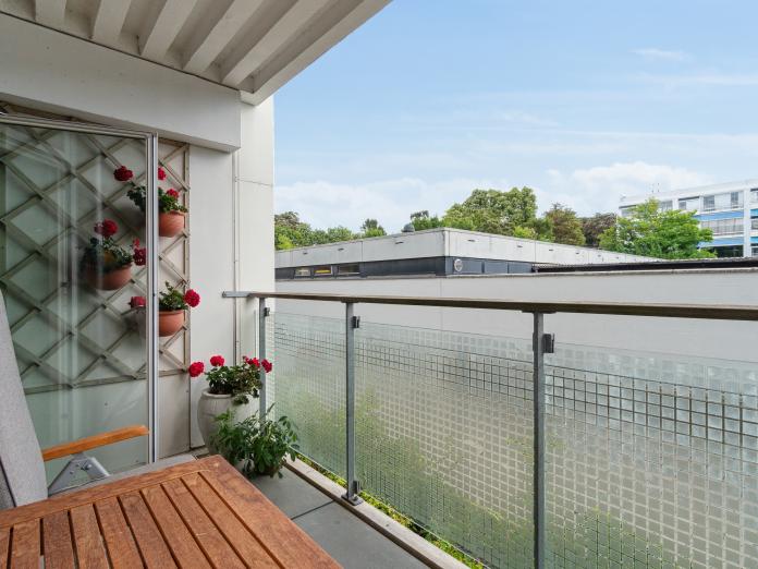 Altan med træbord, stol og krukker med røde blomster.