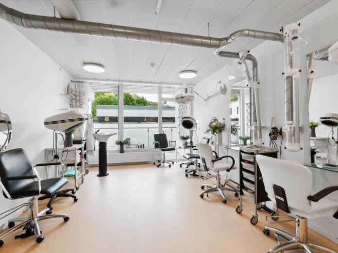 Frisørsalon med stole, frisørgrej, vask og udsugning i loftet.