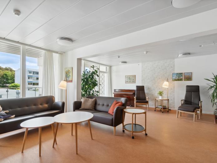 Fælles ste med sofaer, lænestole, sofaborde, planter, vægtapet og billeder.