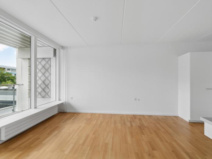 Umøbleret stue med lang vindueskarm, trægulv og skab.