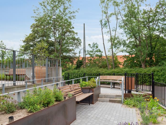 Haveområde med blomsterkasser, bænke, bed og kig til trætoppe.