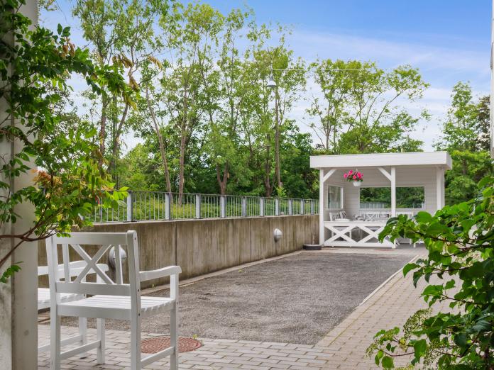 Petanquebane i gråt grus og et par havestole. I baggrunden en overdækket terrasse.